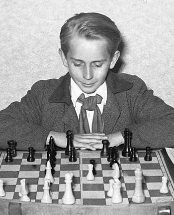 A black and white photograph of a well dressed young man looking at a chess board