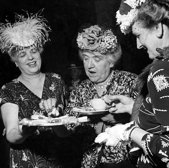 Three old ladies eating and laughing in extravagant hats